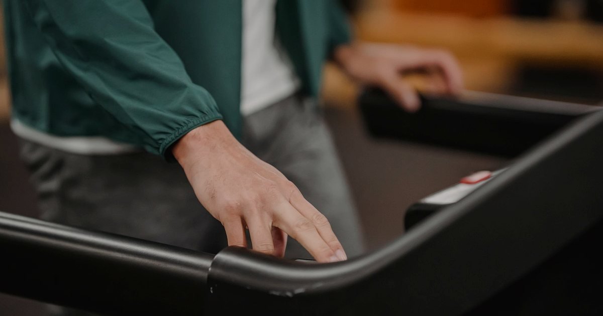 Mão no corrimão de uma esteira para aprender como ligar a esteira