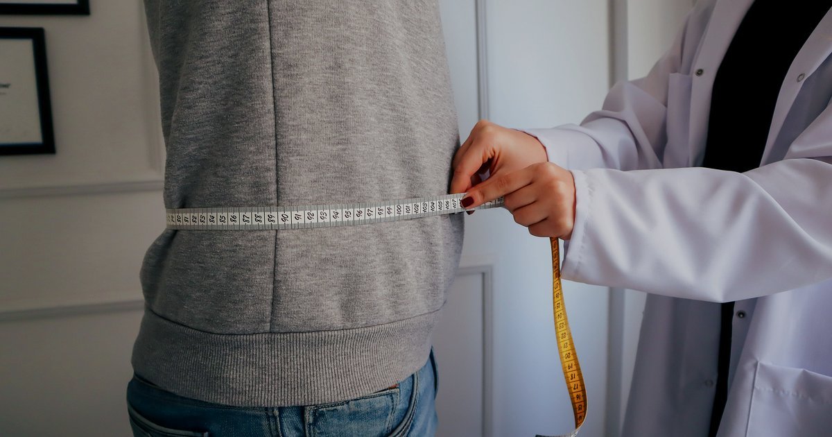 Profissional de saúde medindo a cintura de uma pessoa com fita métrica para avaliar a gordura visceral