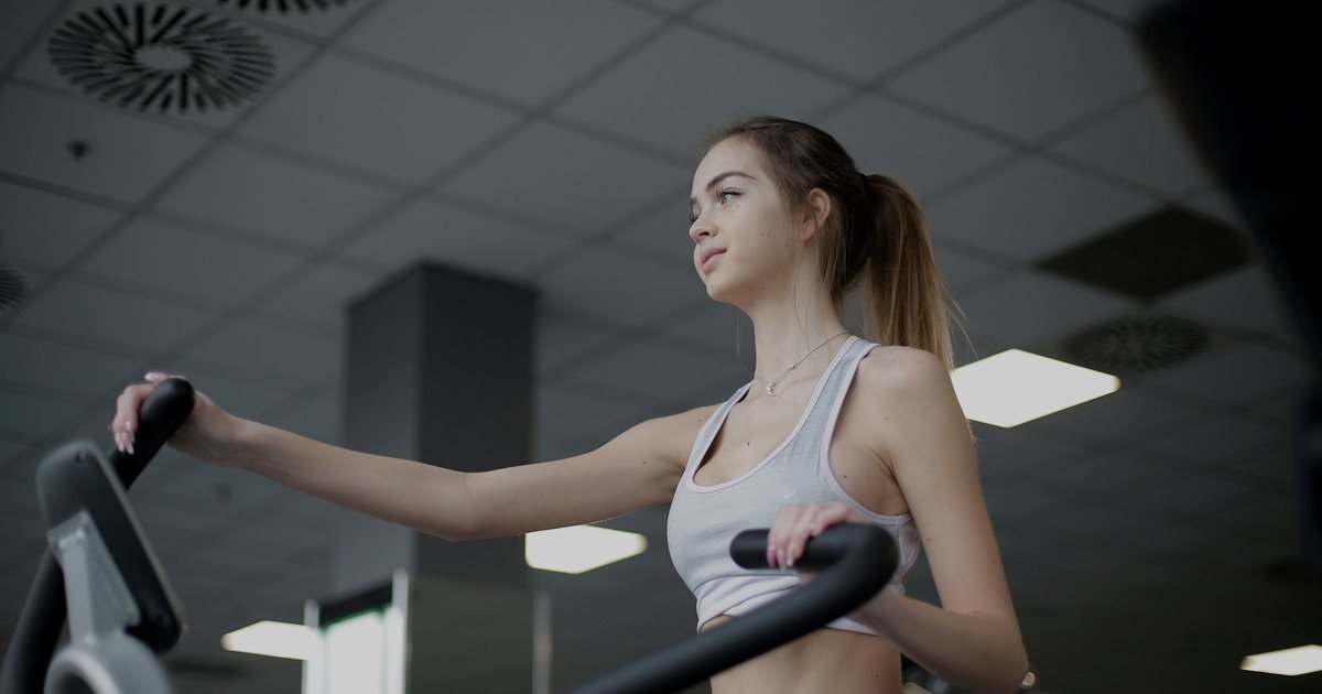 Mulher usando um aparelho de movimento de pernas e braços em uma academia, parecido com um aparelho
