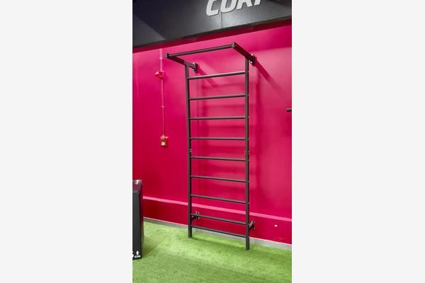 Espaldar de ferro Exercit instalado em academia com parede rosa e piso de grama sintética