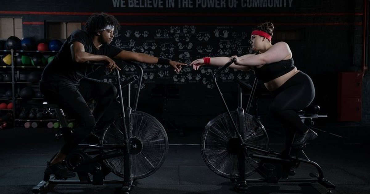 Duas pessoas pedalando em bicicletas ergométricas em uma academia