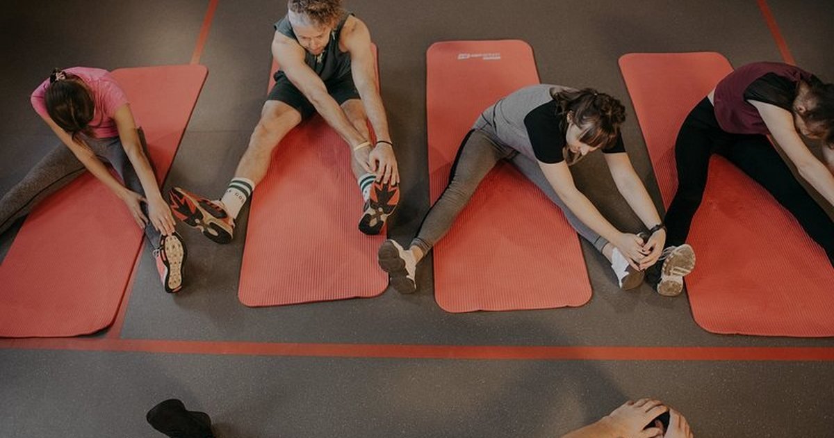 Pessoas alongando as pernas sobre tapetes de ginástica depois do treino