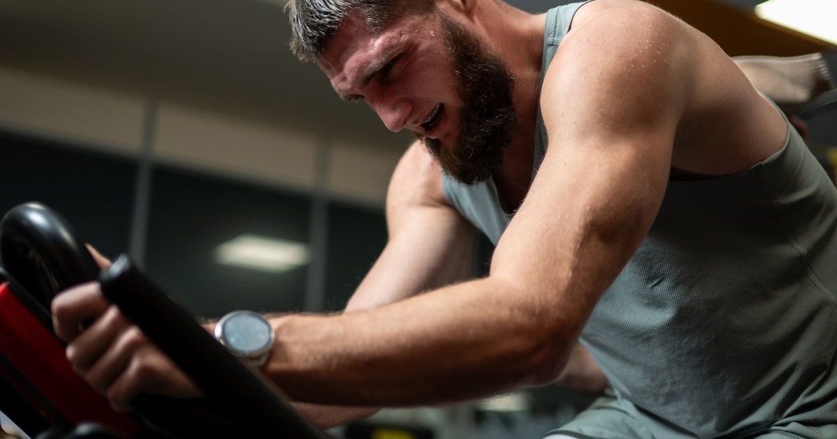 Homem pedalando com esforço em uma bike indoor de academia