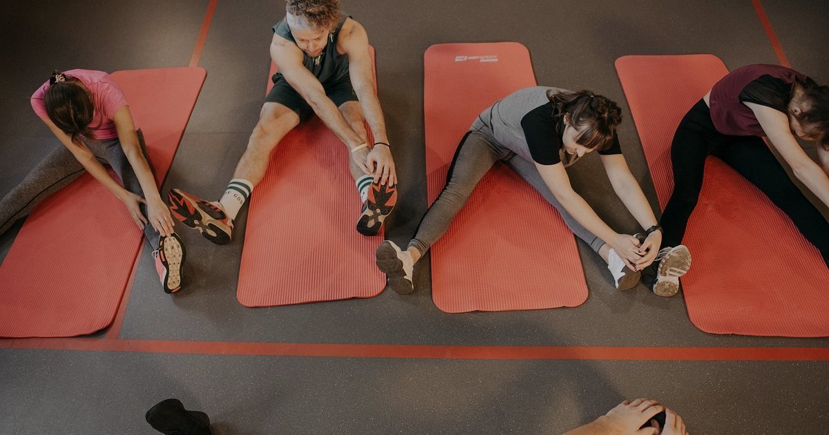 Pessoas alongando-se sentadas em colchonetes vermelhos num espaço de ginástica