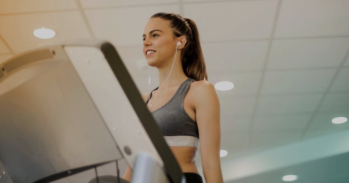 Mulher sorrindo ao usar uma esteira em uma academia iluminada