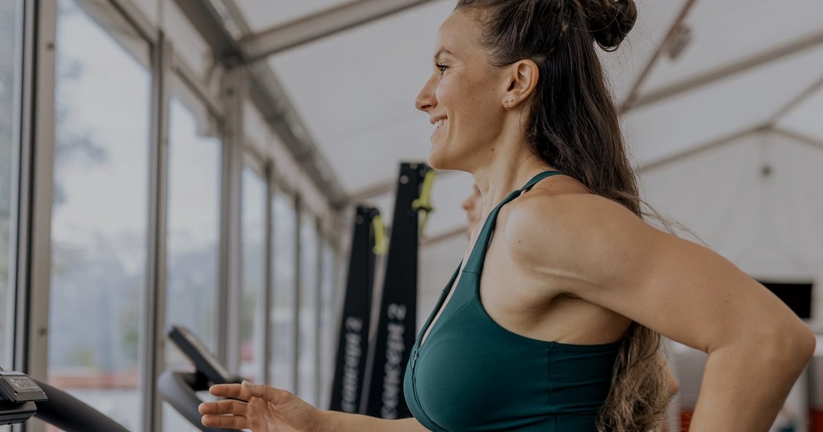 Mulher sorrindo em uma esteira com o celular na mão