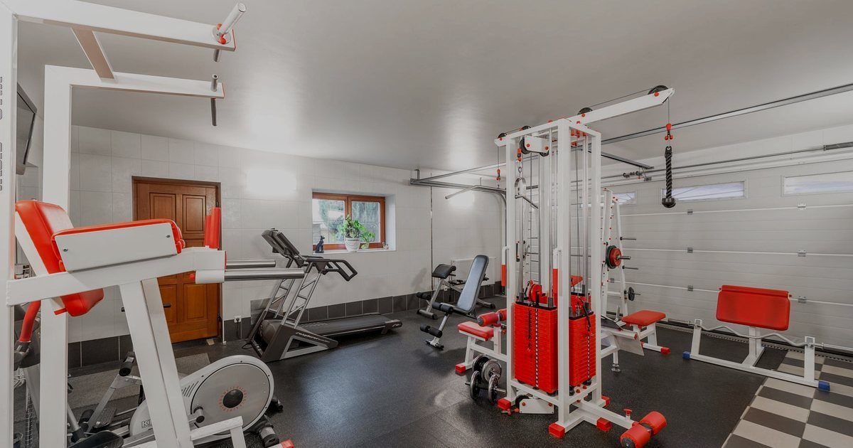 Sala de treino em casa com rack, halteres, bancos e equipamentos de musculação organizados
