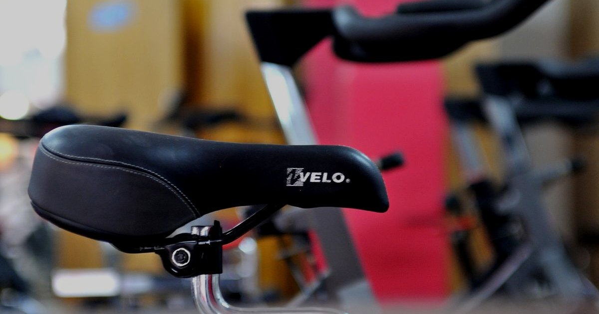 Selim preto de bicicleta de spinning em primeiro plano, com outras bikes desfocadas ao fundo