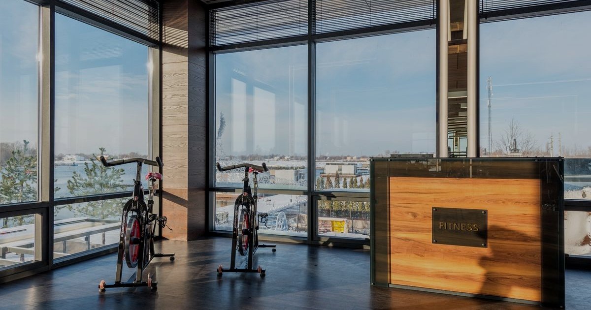 Sala ampla com janelas panorâmicas, duas bicicletas de spinning e um balcão de madeira