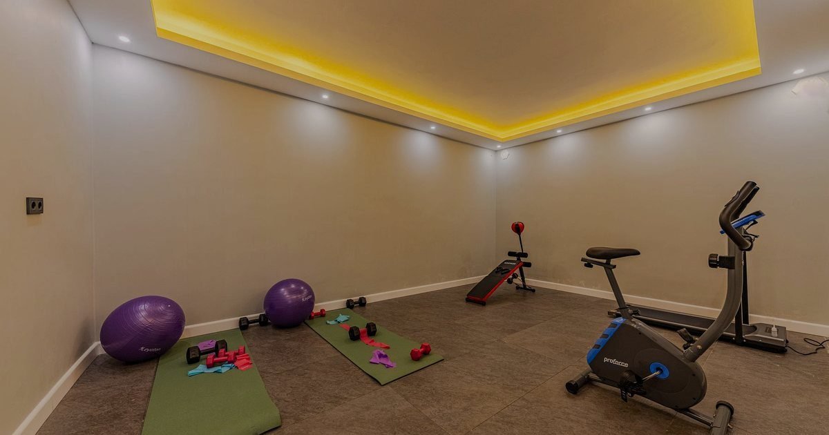 Sala de ginástica em casa com tatame verde, bola roxa e bicicleta ergométrica ao fundo