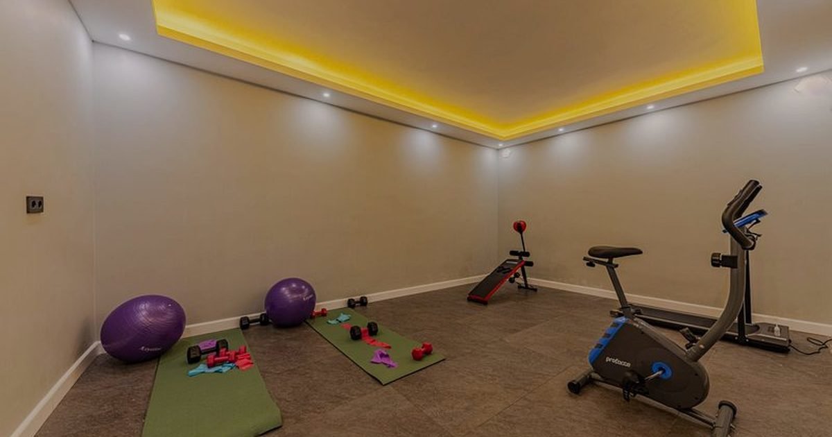 Home gym com tapete, halteres e bicicleta ergométrica ao lado do espaço de treino de força
