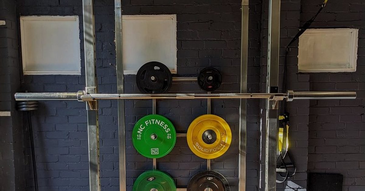 Anilhas coloridas e barras organizadas em suporte numa academia em casa