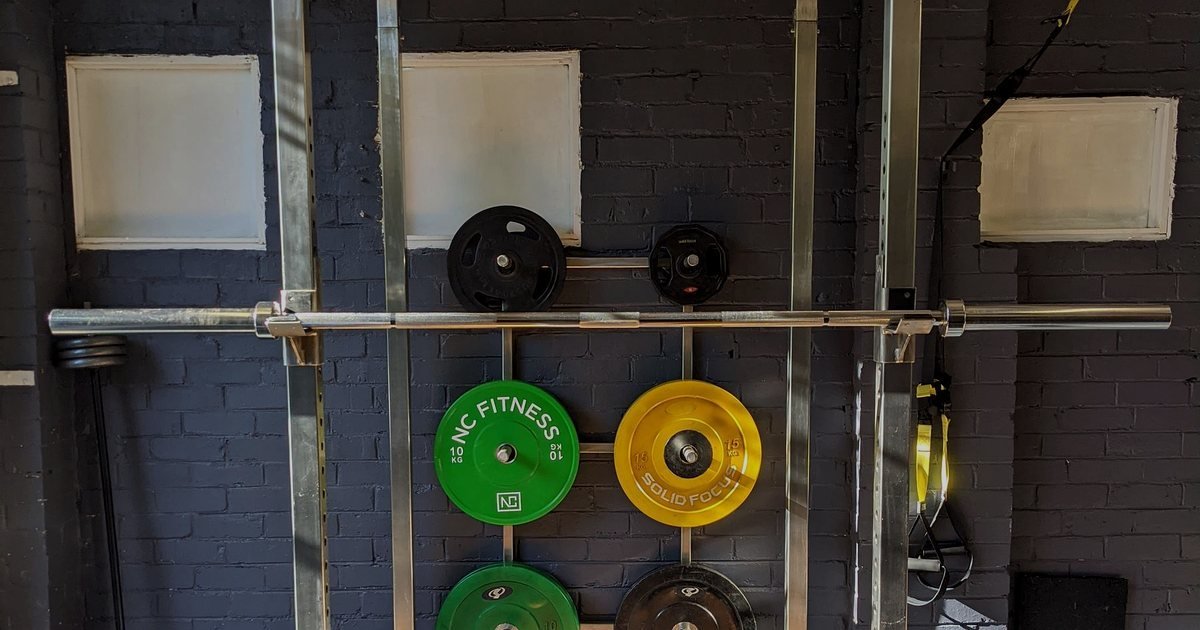 Barra com anilhas coloridas presas em um suporte de academia