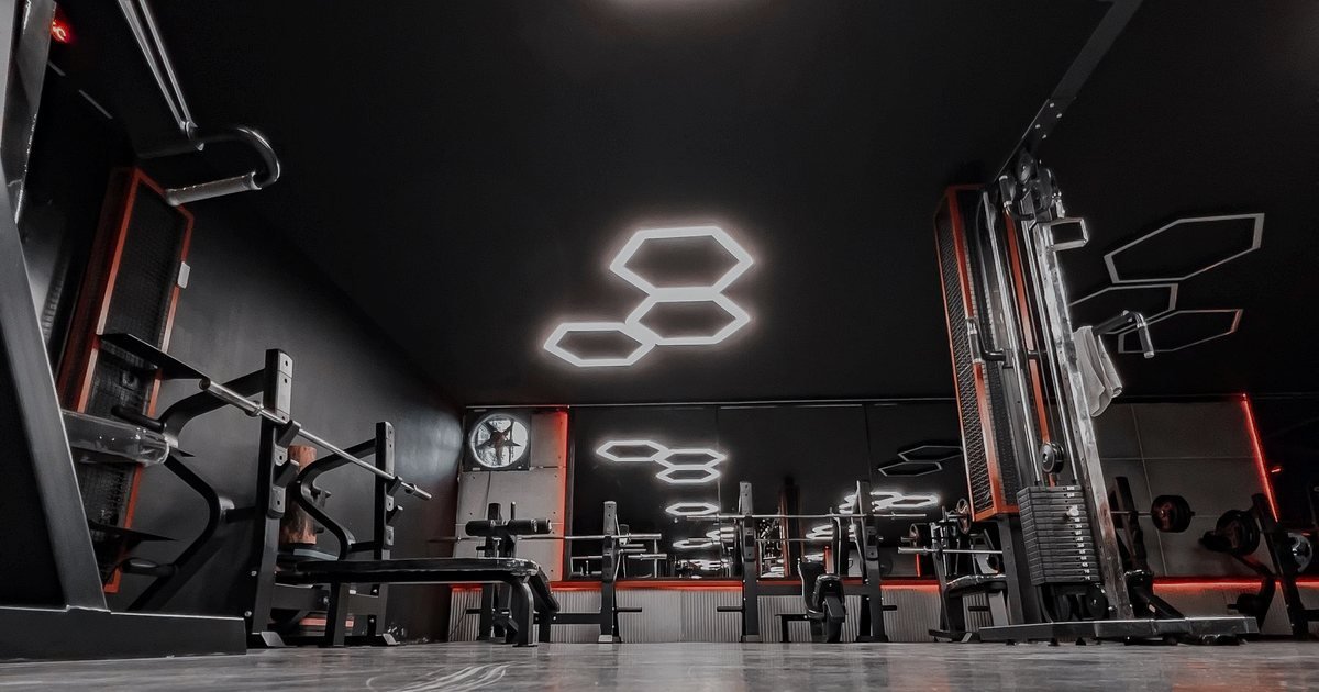 Academia equipada com racks e aparelhos de musculação em tons escuros