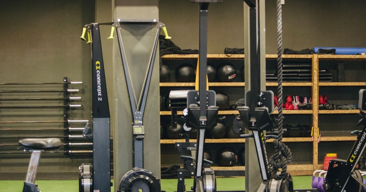 Máquinas de remo em uma academia com prateleiras de equipamentos ao fundo