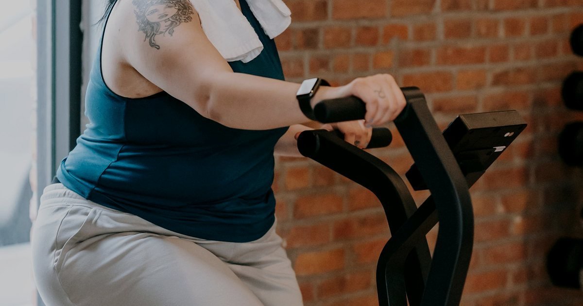 Mulher com o corpo inclinado e as mãos em um aparelho de movimento de pernas em uma academia