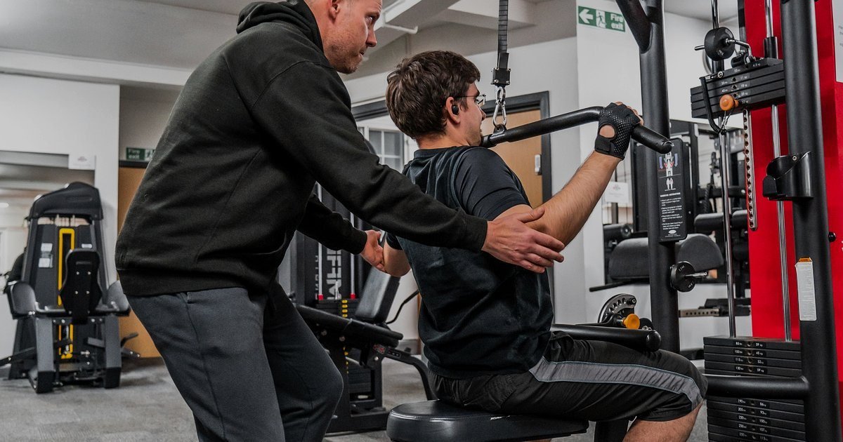 Instrutor orientando um aluno em uma máquina de musculação guiada