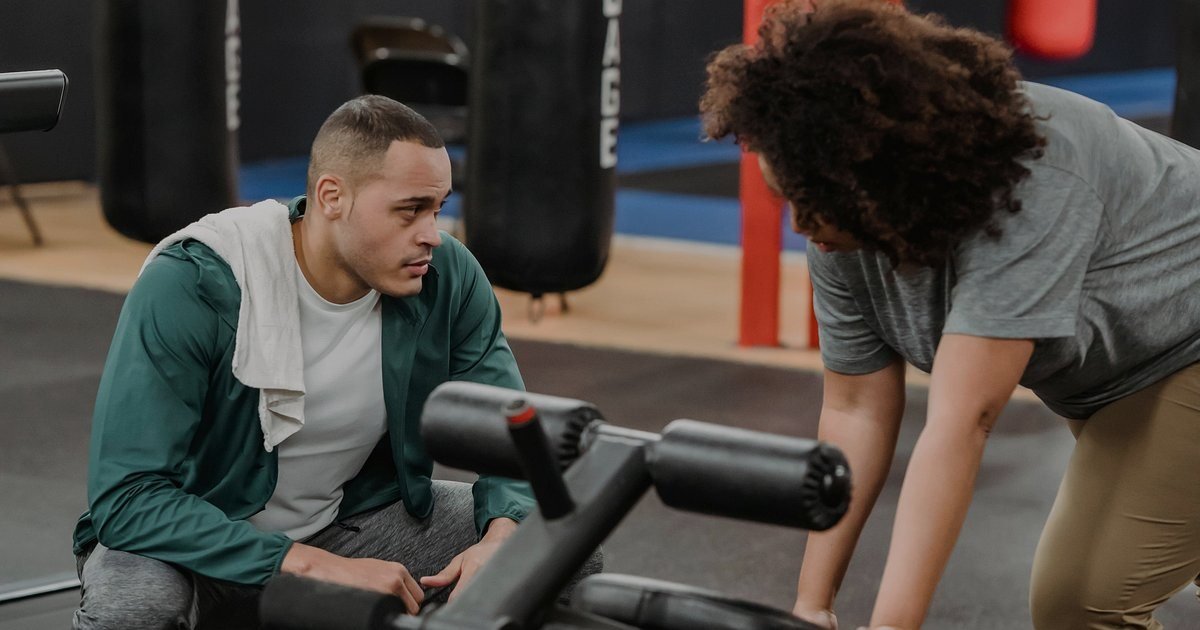 Dois alunos treinando com acompanhamento de instrutor em uma academia